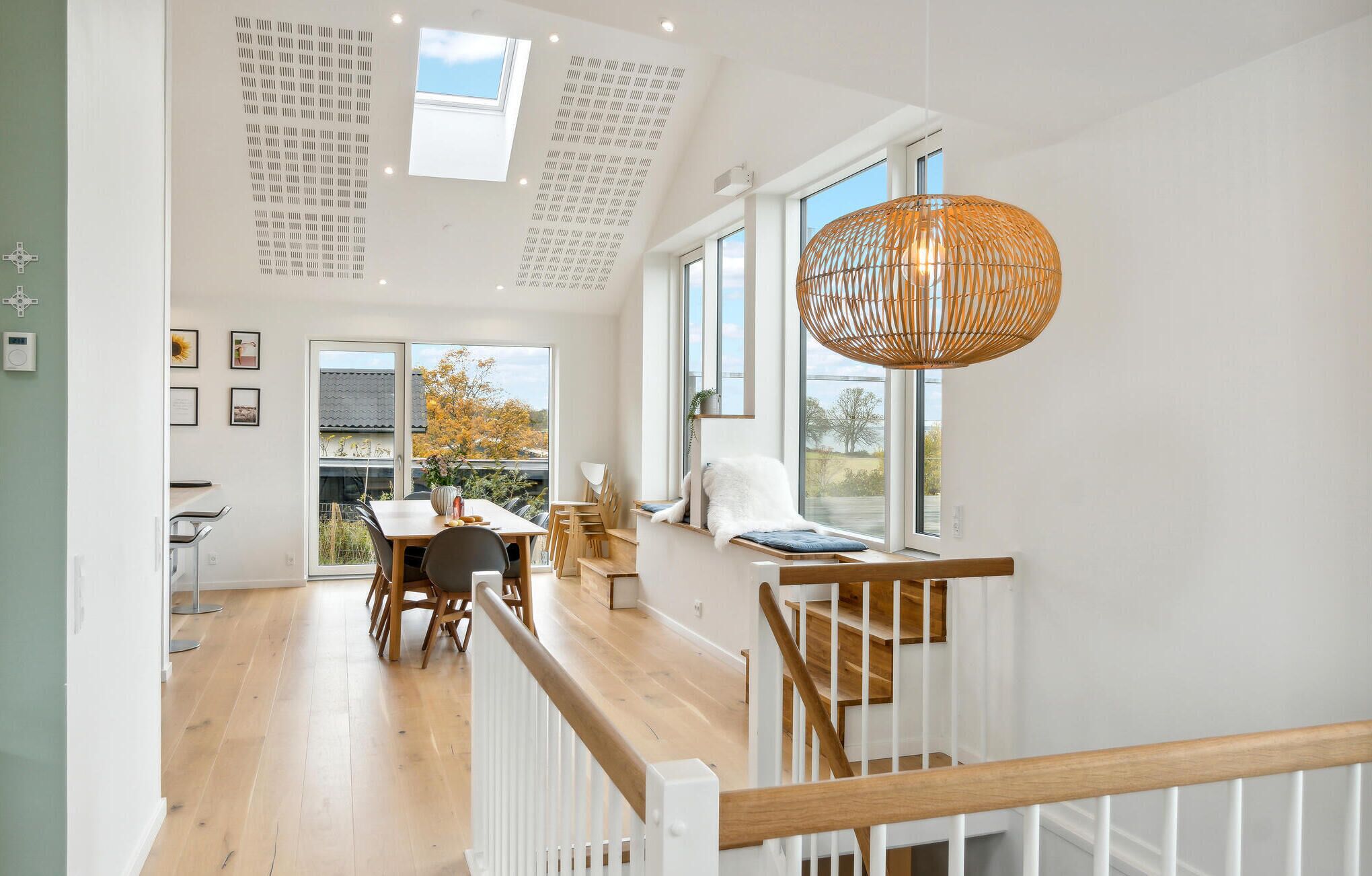 Un interior moderno con comedor, escalera y amplios ventanales que ofrecen vistas al exterior.