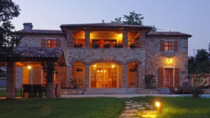 A two-story stone house with a central entrance, a balcony on the upper floor, and a stone pathway leading to the front door.