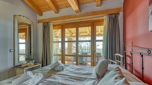 A bedroom with a large bed, a wooden ceiling, a window with curtains, and a red wall.
