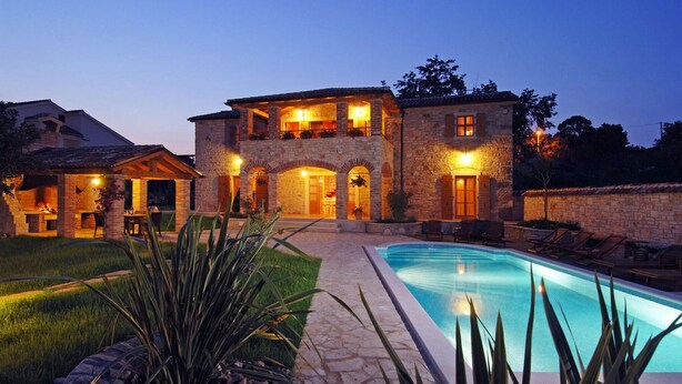 A large stone house with a swimming pool, outdoor seating, and a well-lit patio area.