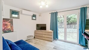 Un salon avec un canapé bleu, un téléviseur posé sur un meuble en bois, une petite table ronde et une porte-fenêtre coulissante donnant sur un espace extérieur.