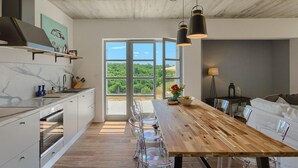 Una cocina moderna con una mesa de comedor de madera, sillas traslúcidas y un ventanal con vistas a la vegetación.