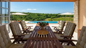 Una mesa de madera con seis sillas, un jarrón de rosas rojas y vistas a una piscina y paisaje verde.