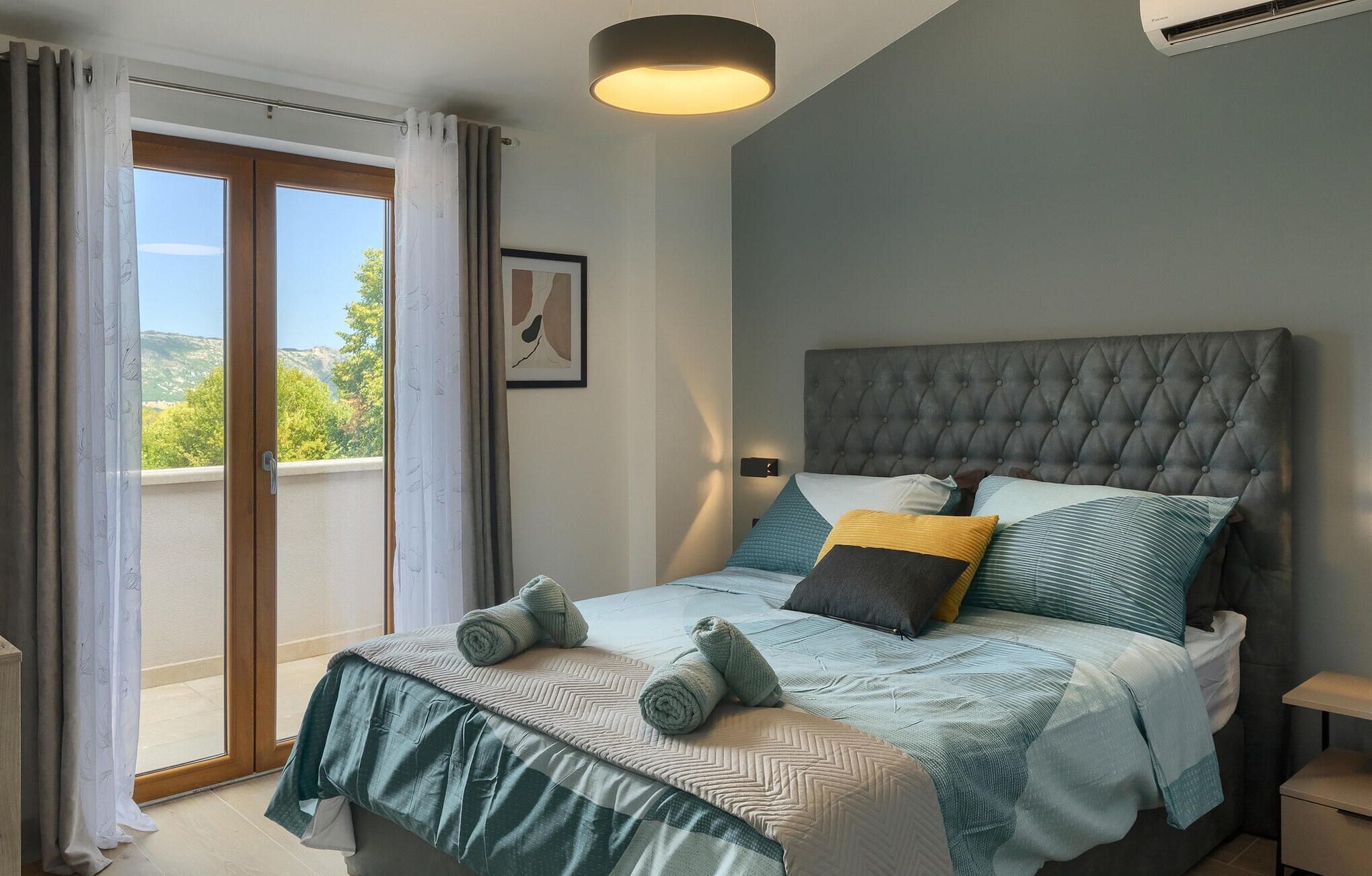 A bedroom with a large bed, a view of the outdoors, and a modern headboard.