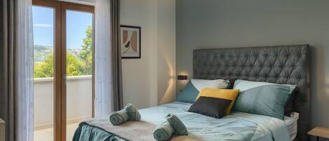 A bedroom with a large bed, a view of the outdoors, and a modern headboard.