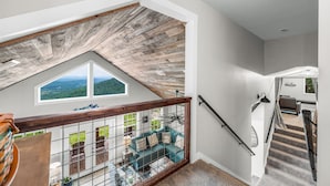 Ein Schlafzimmer im Loft-Stil mit schrägverdeckter Decke, Blick ins Freie, einer Treppe und einer gemütlichen Sitzecke.