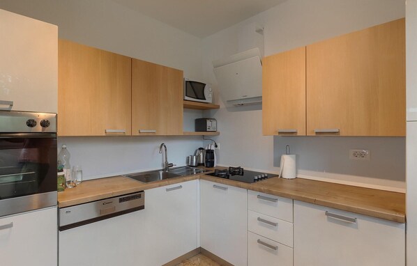 A compact kitchen with wooden cabinets, a built-in oven, a microwave, and a coffee maker.