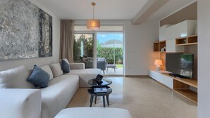 Un salon moderne comprenant un canapé, une table basse, un téléviseur et une grande fenêtre donnant sur un paysage verdoyant et une montagne.