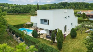 Une maison moderne à deux étages, dotée d’une piscine, entourée de jardins bien entretenus et d’un paysage verdoyant luxuriant.