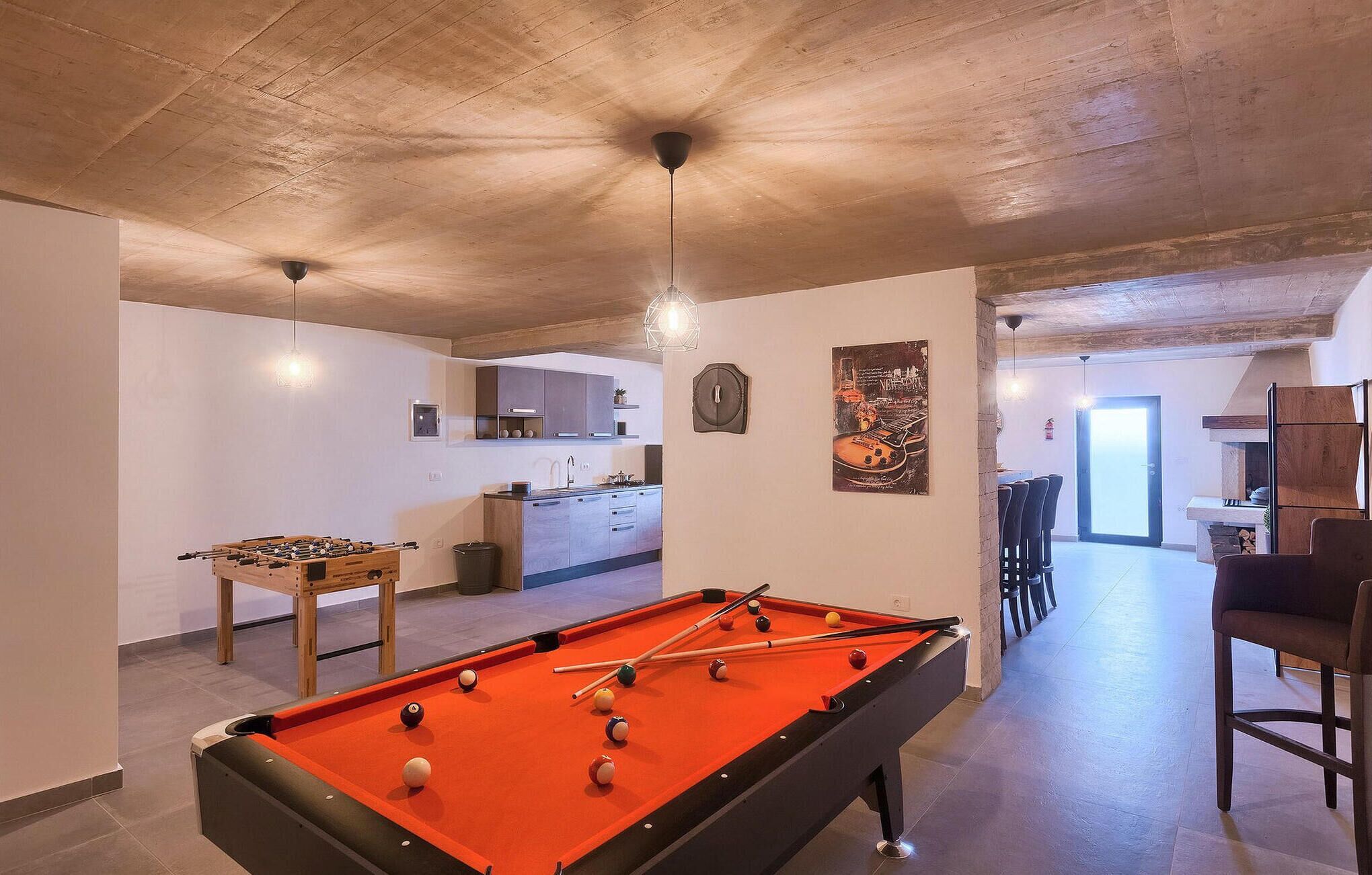 Mesa de billar en una habitación con zona de cocina, comedor y una puerta visible que da al exterior.