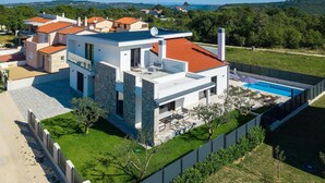 Une maison moderne à deux étages, dotée d’une piscine, entourée d’une pelouse bien entretenue et d’une clôture.