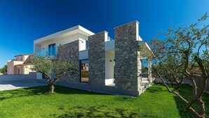 Une maison moderne à deux étages, dotée d’une façade en pierre, d’une pelouse bien entretenue et surplombée d’un ciel bleu azur.
