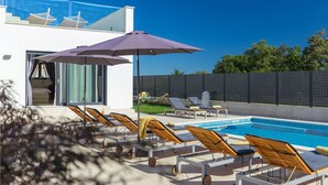 Un espace aménagé au bord de la piscine, avec des chaises longues, un grand parasol et une vue sur un bâtiment moderne à la façade en verre.