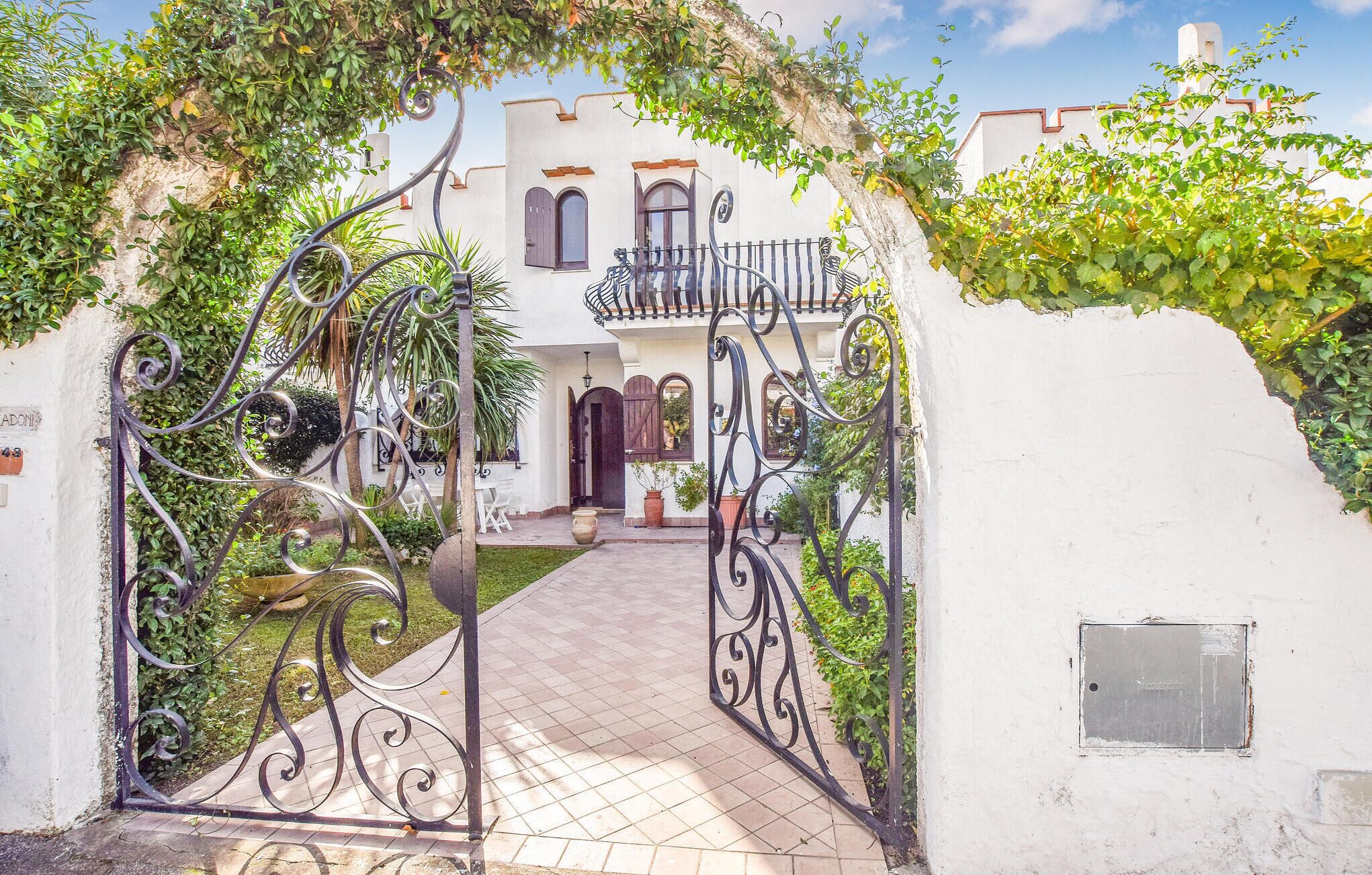 Una entrada con reja de hierro forjado y un camino que conduce a un edificio de fachada blanca y ventanas en arco.