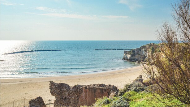 A coastal beach with a rocky cliff and a clear view of the sea.