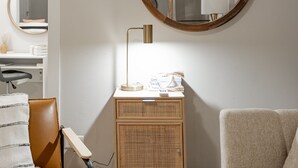 Una habitación con mesita de noche, lámpara, espejo y una silla.