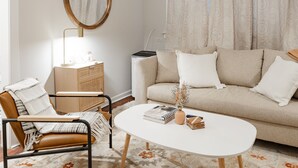 Una sala de estar con sofá, mesa de centro, sillón, aparador de madera y espejo.