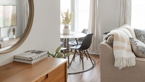A modern living room with a round dining table, black chairs, a wooden side table, and a beige sofa with a striped throw. - Stylish and Comfy Studio near Loyola Park (Chicago)