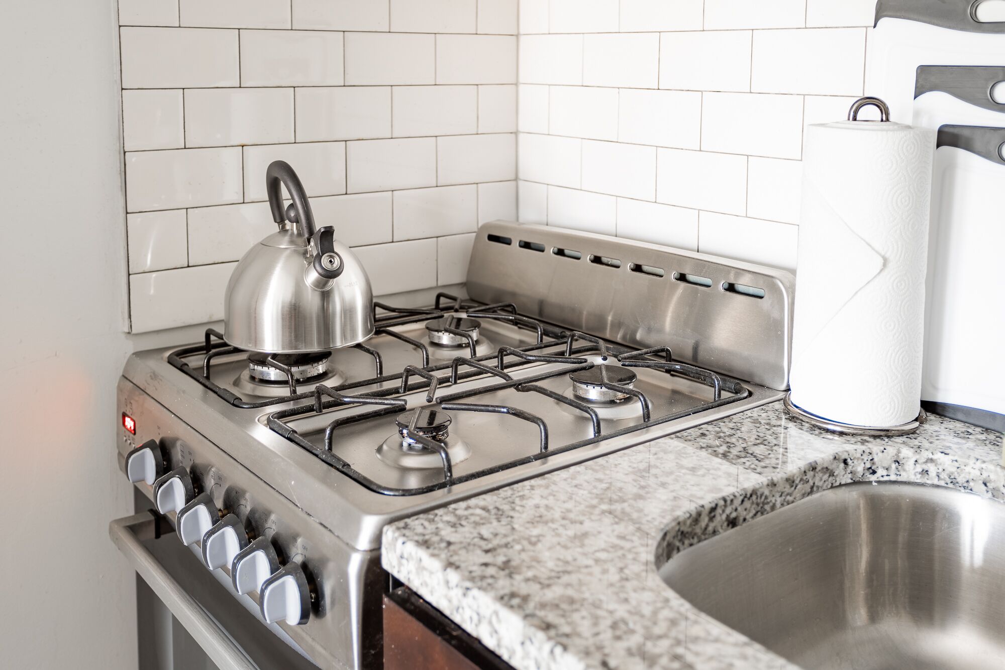 A kitchen with a stainless steel stove, a kettle, and a sink.