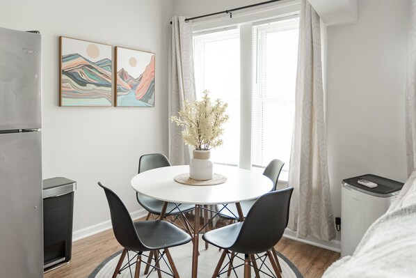 A modern kitchen with a refrigerator, a dining table with chairs, and a window with curtains.