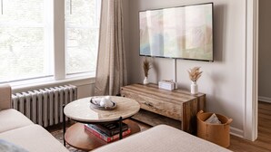 A modern living room with a round coffee table, a sofa, a TV mounted on the wall, and a radiator. - Stylish and Comfy Studio near Loyola Park (Chicago)
