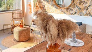 Une pièce comprenant un fauteuil en osier, un pouf rond en fibres tressées, un vase contenant des plantes séchées et un miroir accroché au mur.