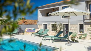 Une maison moderne à deux étages, dotée d’une piscine, d’un espace extérieur aménagé et d’une façade en pierre.