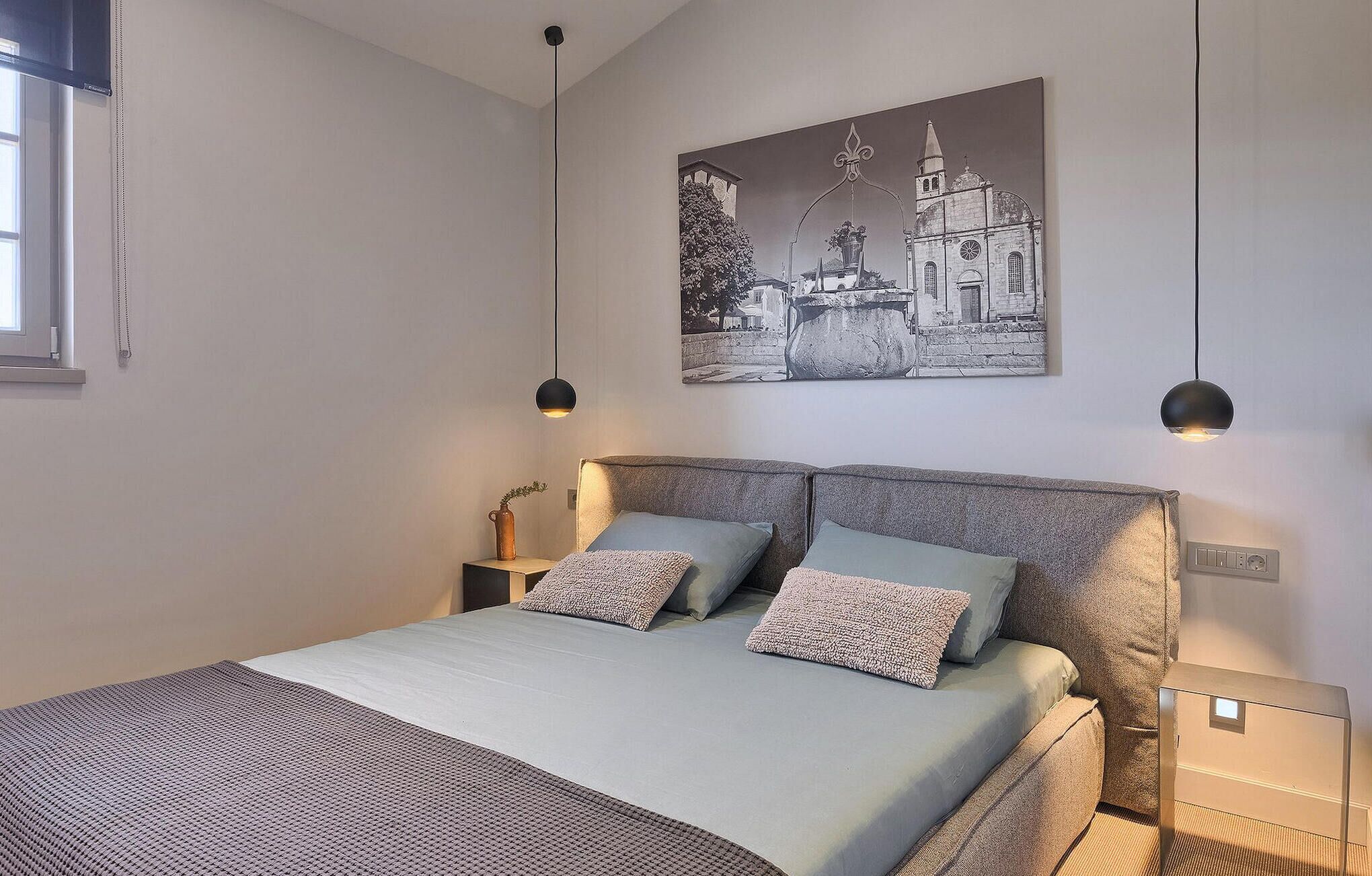 A modern bedroom with a large bed, two bedside tables, a wall-mounted artwork, and pendant lighting.