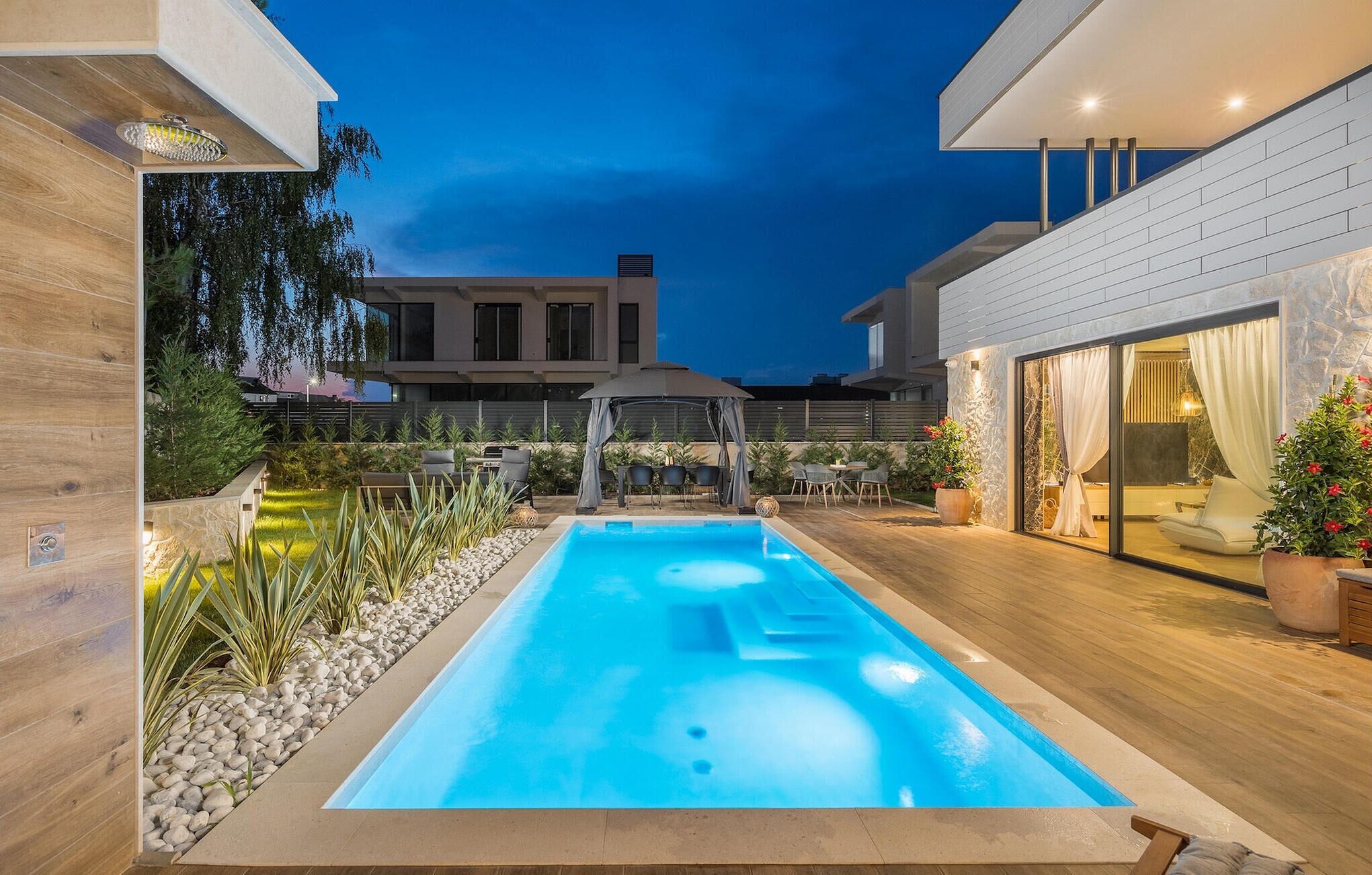 Un espace piscine extérieur moderne, doté d’un jacuzzi, entouré d’une terrasse en bois et d’un mur en pierre.