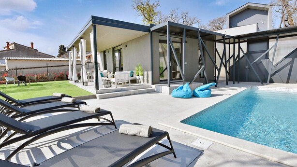 Un área de piscina moderna al aire libre con sillas de descanso y una zona de estar cubierta.