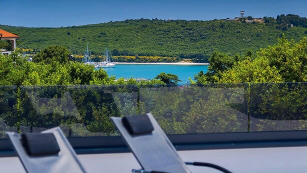 Ein Balkon mit Blick auf eine Küstenlandschaft, darunter ein Strand und Segelboote.