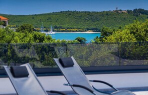 Ein Balkon mit Blick auf eine Küstenlandschaft, darunter ein Strand und Segelboote.