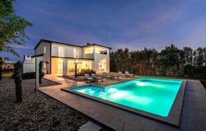 Ett modernt hus i två våningar med en swimmingpool, en uteplats och en välskött trädgård.