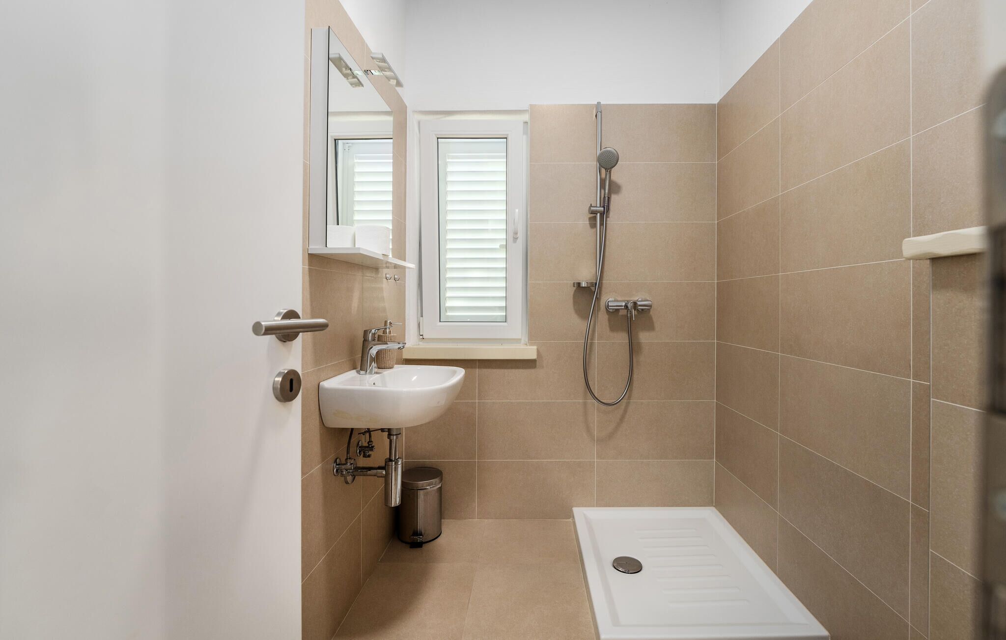 A small, modern bathroom with a sink, mirror, window, shower, and toilet.