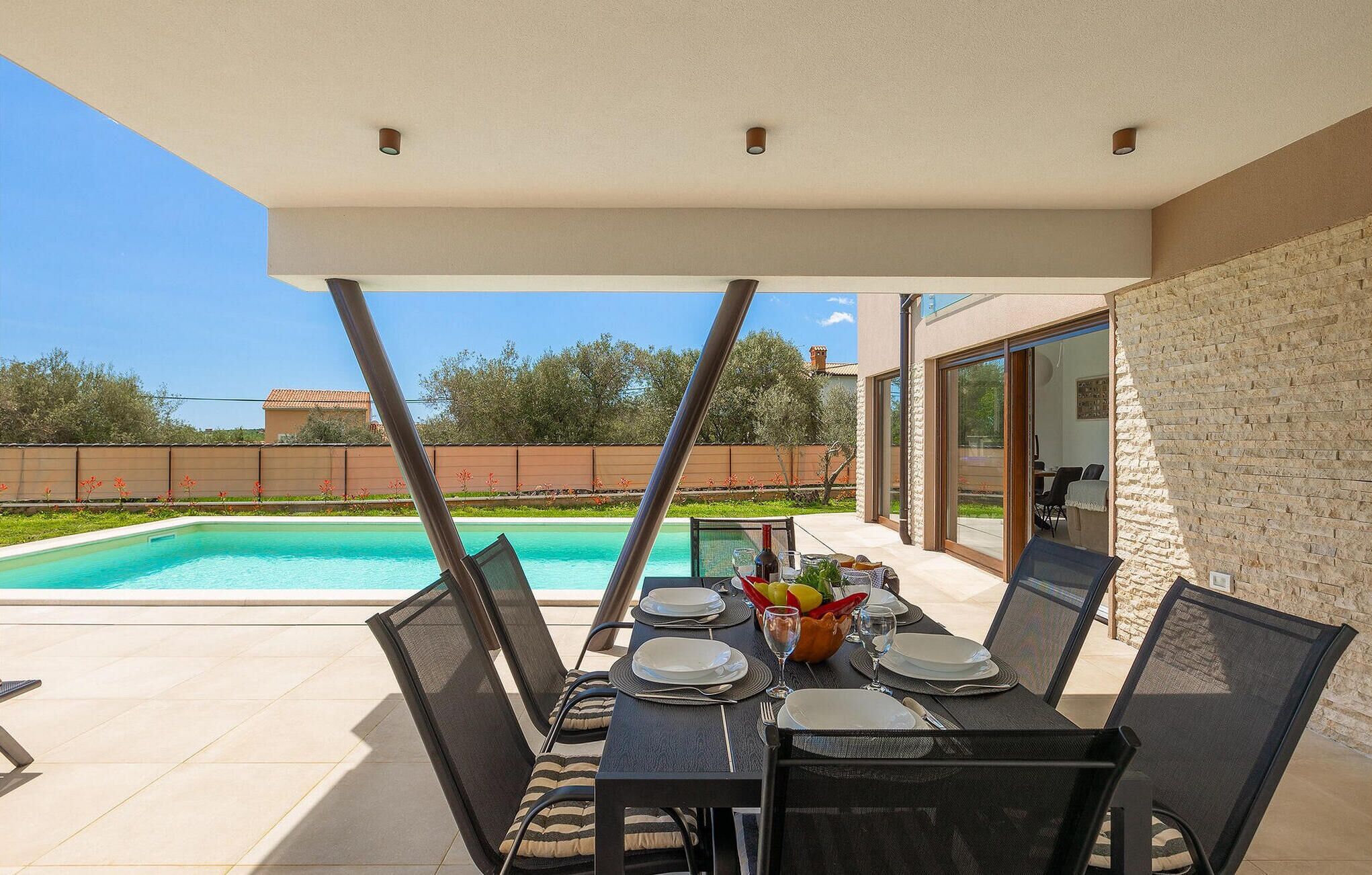 An outdoor dining area with a pool view, a table set for two, and a stone wall.