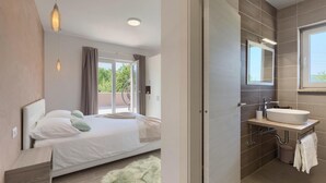 A modern bedroom with a large bed, a view of the outdoors, a bathroom with a sink and mirror, and a fluffy rug. - Awesome home in Pazin with sauna (Pazin)