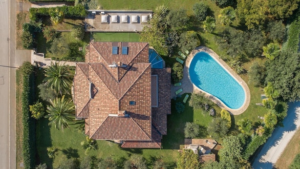 An aerial view of a house with a swimming pool, surrounded by lush greenery and palm trees.