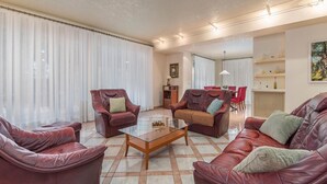 A living room with leather sofas, a glass coffee table, and a dining area with red chairs.