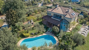 A large house with a swimming pool, surrounded by lush greenery and a well-maintained garden.