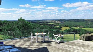 Un terrazzo in legno con tavolo e sedie, affacciato su un paesaggio verde con colline e alberi.