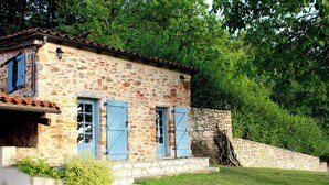 Un edificio in pietra con due persiane blu, una scala in pietra e un muro in pietra.