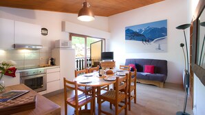 A modern kitchen with white cabinets, a dining table set for four, and a large window. - Au calme & au coeur de la station | 50m remontées (Les Deux Alpes)