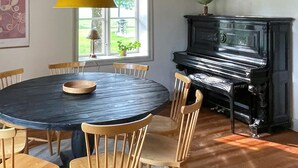 Un coin repas avec une table ronde et des chaises en bois, un piano noir et une fenêtre donnant sur un paysage verdoyant.