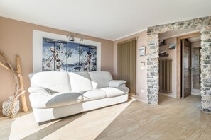 A modern living room with a white sofa, a painting on the wall, and a stone archway leading to a door. - Exceptional apartment of approximately 50 m2, located on the ground floor of a residential complex along the coast of the Gulf of Poets! The accommodation offers sea view, private garden, 2 bedrooms and outdoor dining area!The apartment is located in Fia (Tellaro, Lerici)