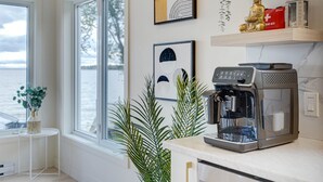 A modern kitchen with a coffee machine, a view of the sea, and decorative wall art.