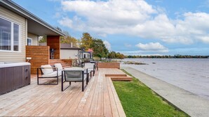 A deck with outdoor furniture and a hot tub, overlooking a lake.