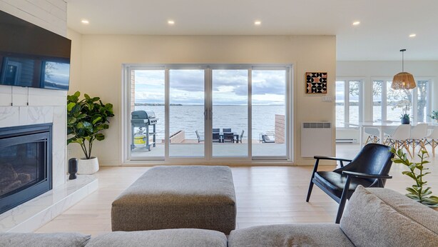 A modern living room with a fireplace, a large sliding glass door to a patio, and a view of the water.