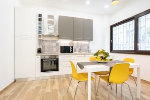 A modern kitchen with white cabinets, a microwave, and a dining area with a table and yellow chairs.