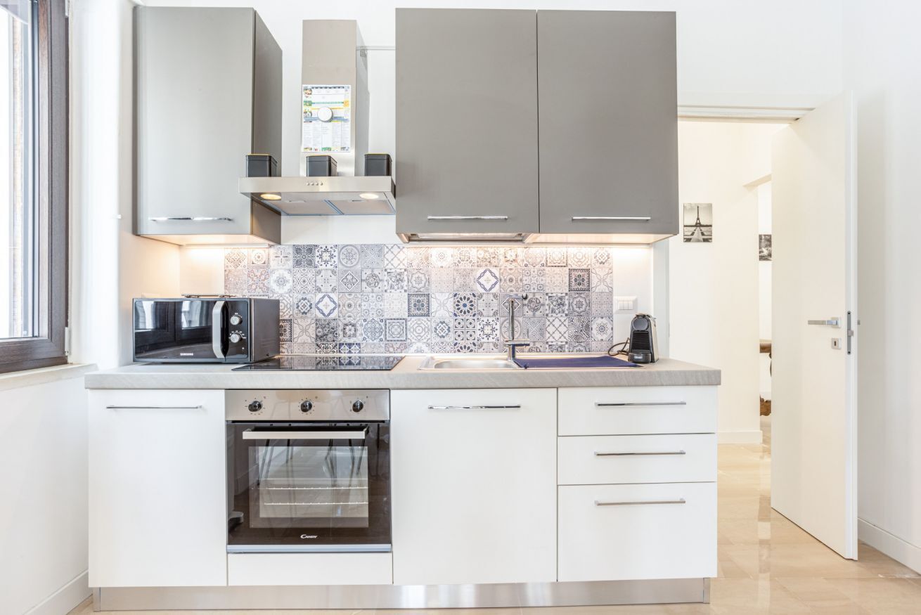 Una cocina moderna con armarios blancos, horno empotrado, microondas y un salpicadero con diseño.