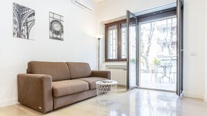A modern living room with a sofa, a round coffee table, and a glass door leading to an outdoor area with a table and chairs. - GuestHost - Vomero Deluxe Paris with terrace (Napoli)